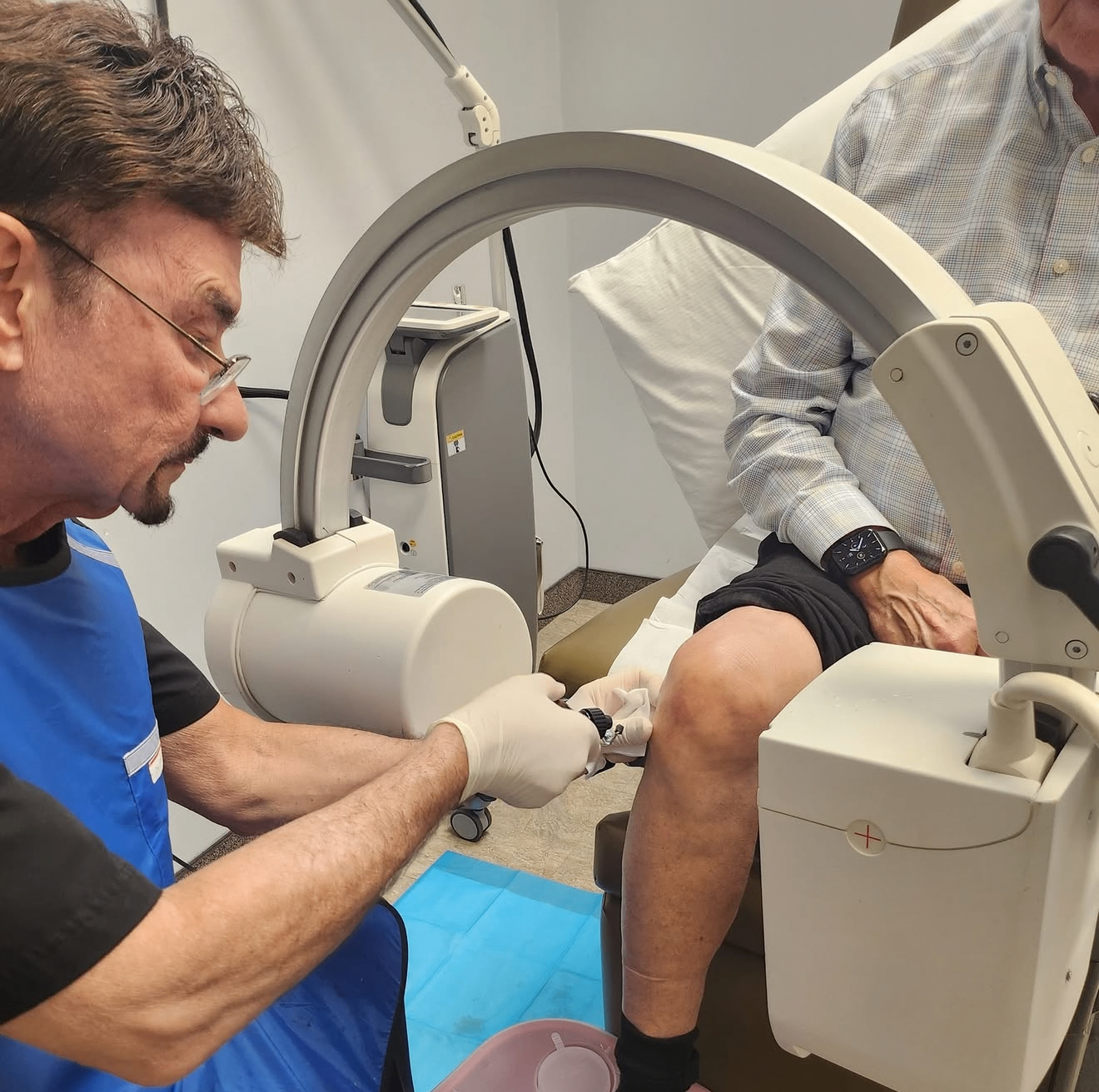 Dr. Fretta providing in-office care to a patient's knee alongside treatment equipment